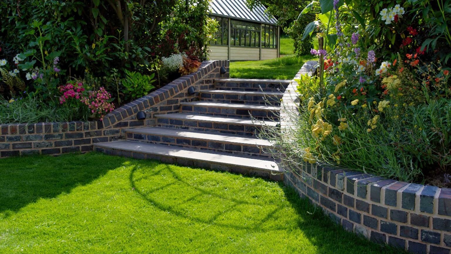 Straight garden steps in a delta configuration connecting two lawn terraces with black brick risers and retaining walls.