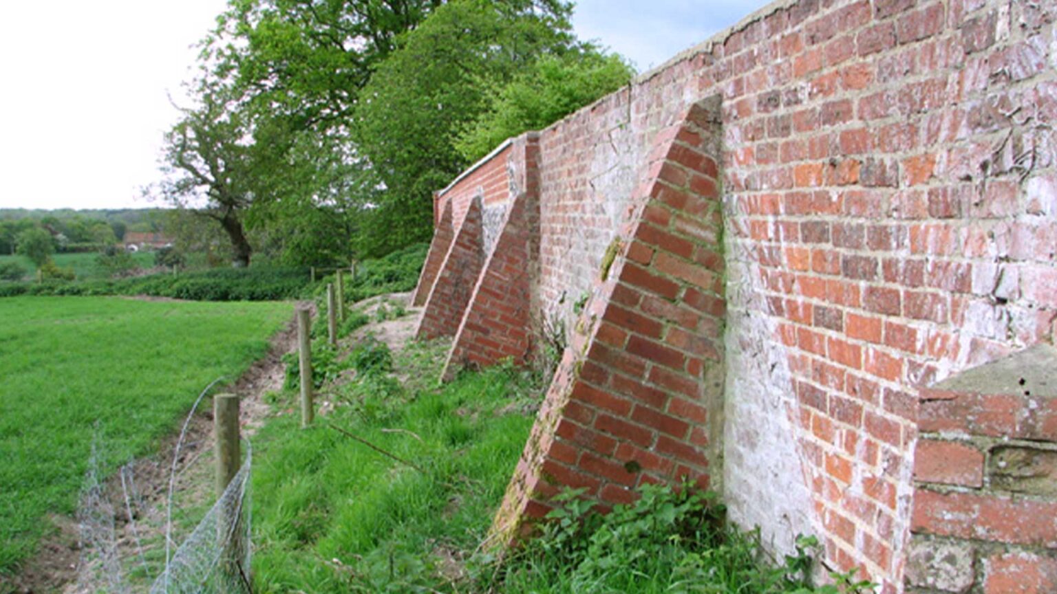 The backside of a buttresses red brick wall. The buttressing is designed to prevent kickout.