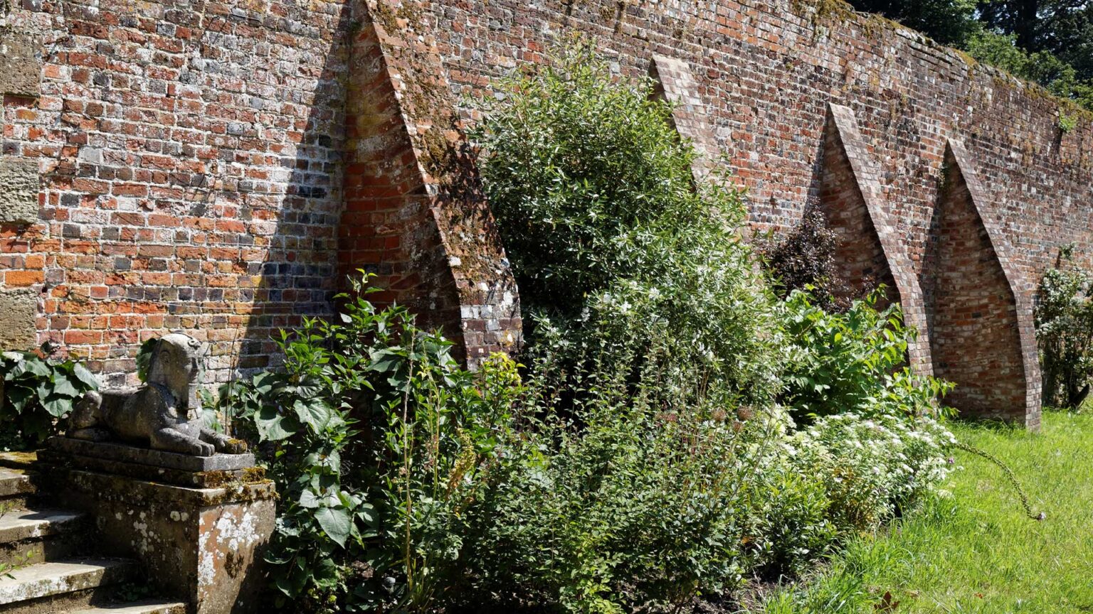 A buttressed high red brick retaining wall supporting terraced sections of this garden.