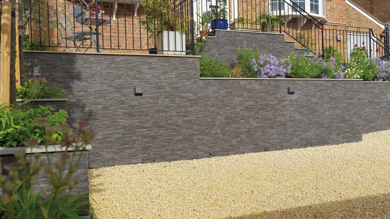 The dramatic use of porcelain stone-effect cladding on the terraced walled entrance to this traditional country redbrick house.