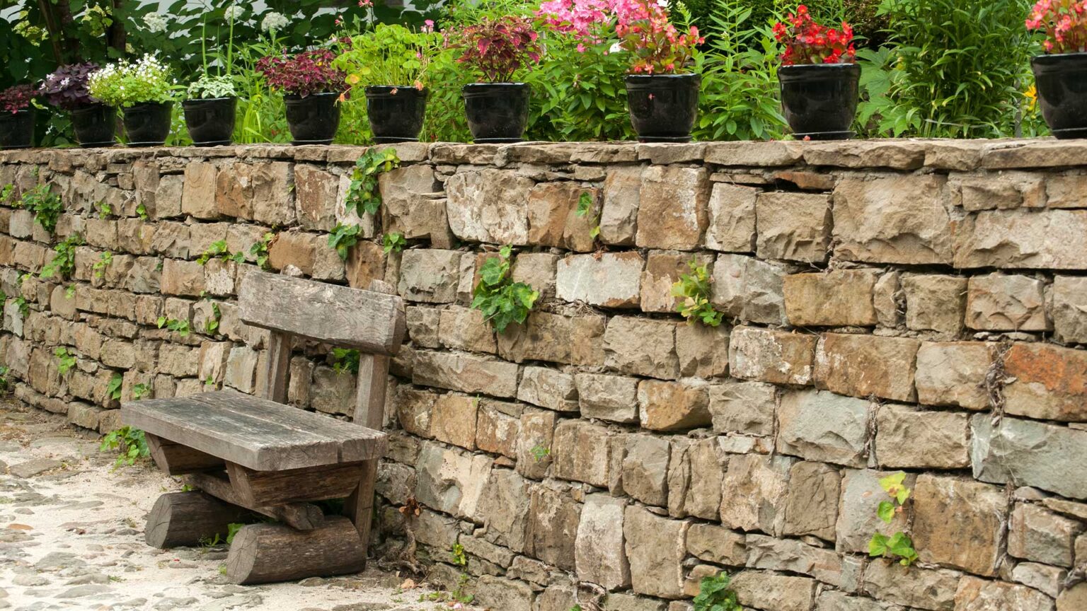 An unbound dwarf retaining wall (with bound coping stones). The stones are rough hewn and dressed, for a rustic aesthetic.