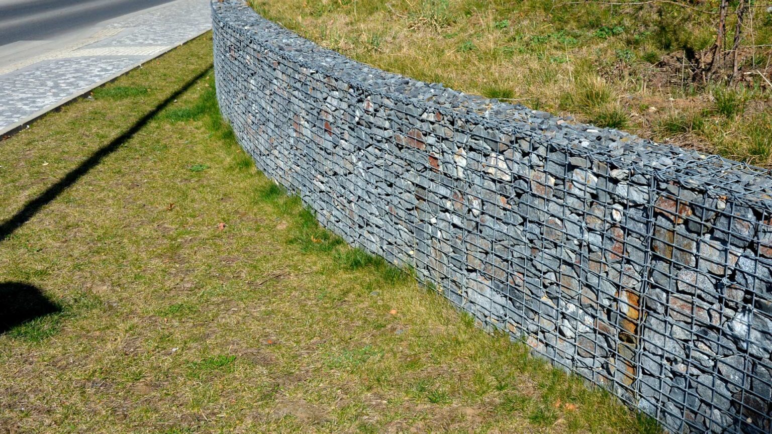 A gabion cage retaining wall filled primarily with angular shaped limestone rocks that interlock well for stability.