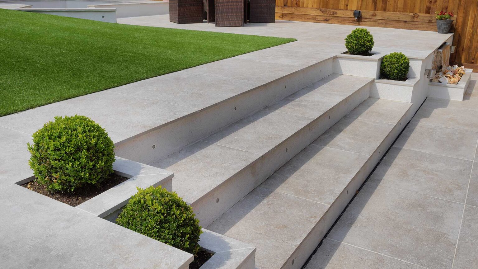 Minimalist porcelain paving steps with lighting in the face of the lifts and raised beds with topiary on either side.