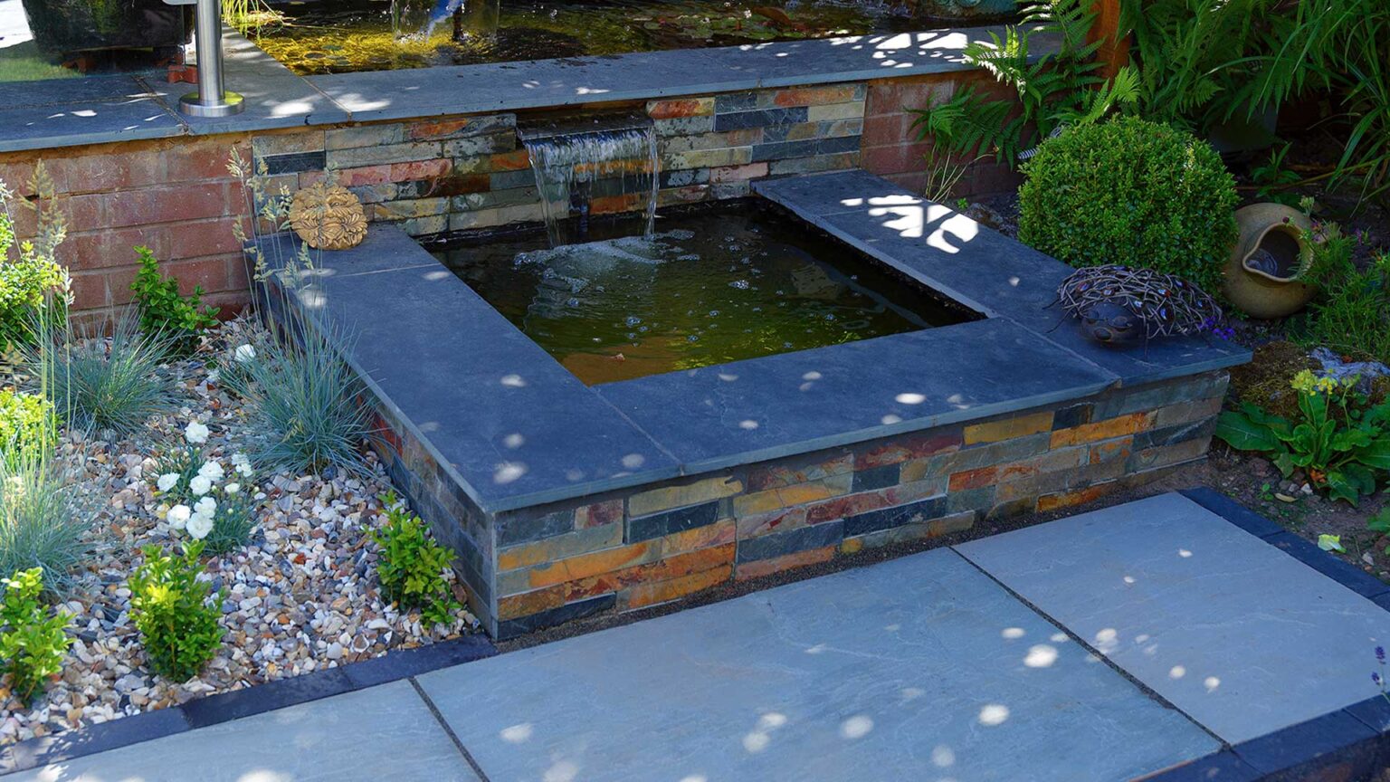 A knee wall clad in rusty slate cladding used to create a pond with black slate coping/seating