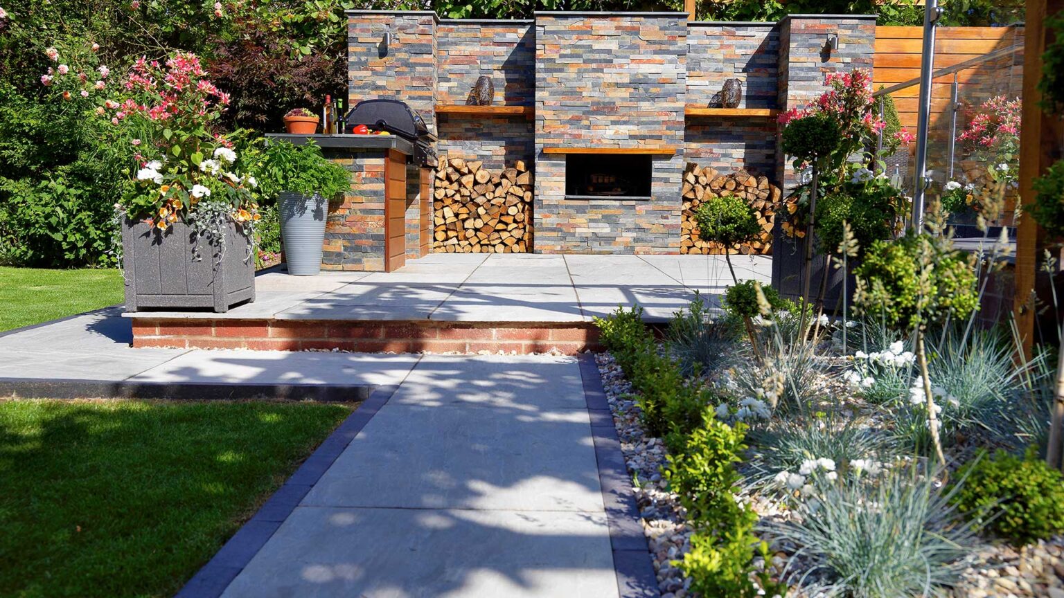 An outdoor kitchen wall and carcase clad with rusty slate stone slips that works beautifully with the colour palette of slate and wood used elsewhere.