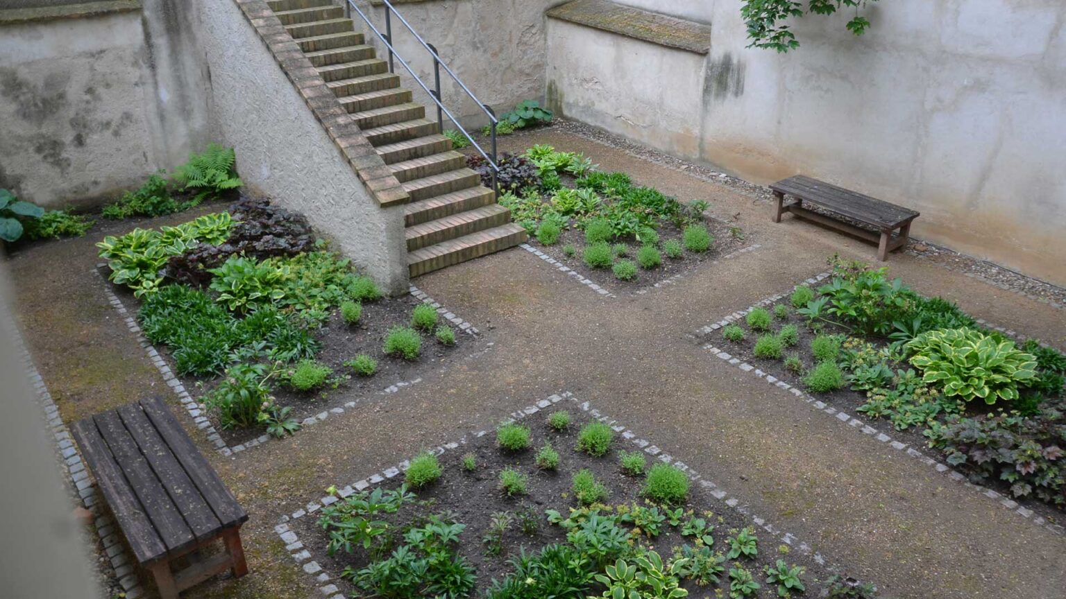 A sunked courtyard garden with a symetrical layout and high surrounding retaining walls with a white rendered finish.